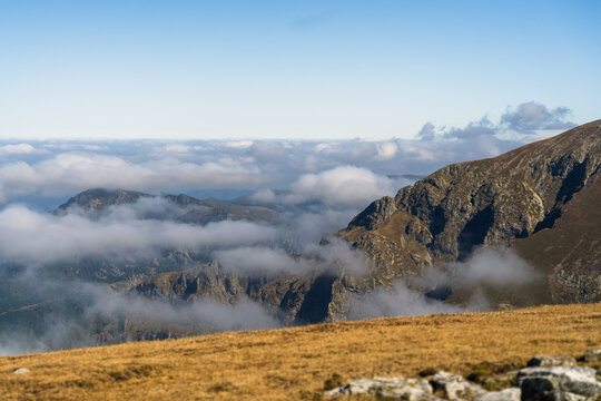 View of Botev Peak in the Balkan Mountains with rocky slopes, golden alpine grass, and clouds drifting through the valleys in Balkan Mountains, Lovech, Bulgaria.