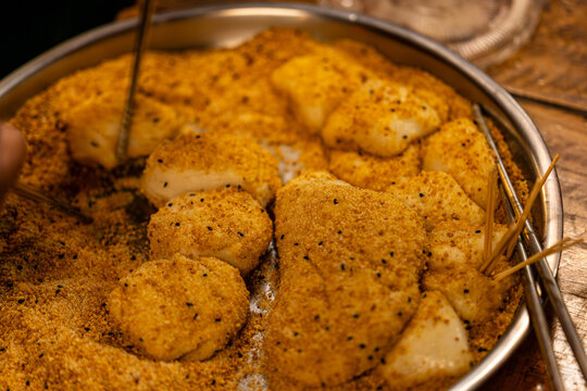 Hakka mochi, made with peanut powder and sesame coating, served on an iron pan with bamboo skewers, is a traditional ethnic dessert.