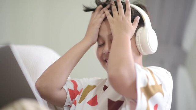Frustrated Asian schoolboy experiencing migraine and exhaustion during difficult digital online education course. Overwhelmed preteen pupil showing severe study burnout