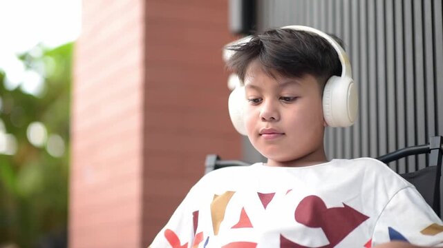Thoughtful Asian schoolboy wearing wireless headphones listening to digital audio edtech course outdoors. Smart preteen pupil thinking deeply about future education lesson