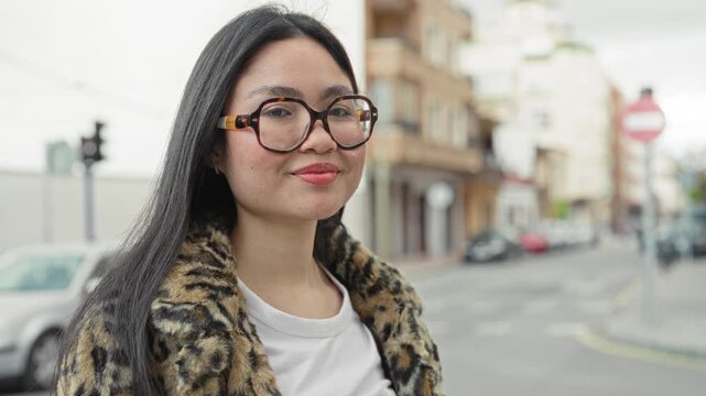 Woman wearing tortoiseshell glasses and leopard coat smiles with visible face and earring on a city street; confidence youthful spirit.