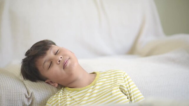 Exhausted Asian schoolboy leaning back and falling asleep on comfortable sofa after intense online education course. Tired preteen pupil resting from heavy academic homework assignment