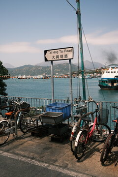 View of Tai Hing Tai Road street sign with parked bicycles and a waterfront harbor view with boats in Hong Kong, Hong Kong.