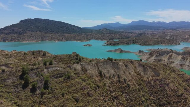 Drone aerial view of Embalse de Negrat&iacute;n with turquoise waters, rugged hills and distant mountain ranges in Andalusia, Spain