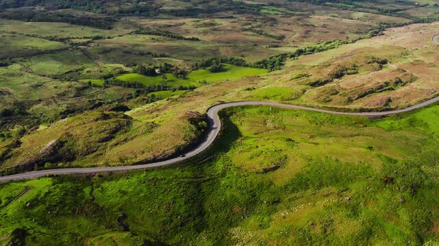 Aerial standstill view of a lone car driving along a winding road through County Kerry highlands