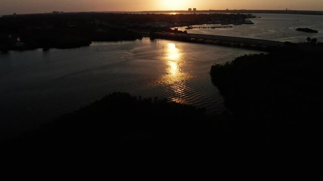 Setting sun reflects in a bright path on Braden River as a low bridge spans the inlet and mangrove peninsulas sit in shadow.