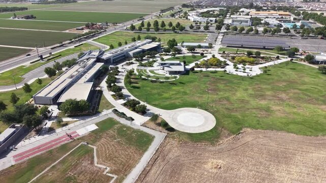 Tracking aerial perspective showing the modern campus architecture of the College of the Sequoias, surrounded by lush green lawns, manicured gardens, and adjacent agricultural farmlands