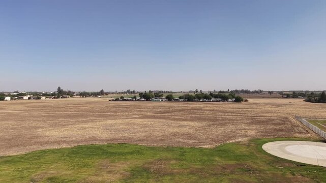Drone perspective rising above the rural landscape surrounding the College of the Sequoias in Visalia, California, showing dry fields transitioning into green farmland on a clear day