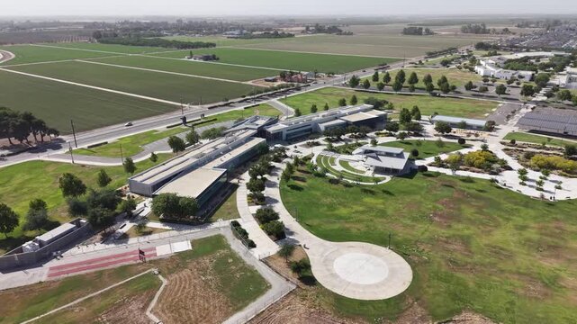Aerial push in shot of the modern architecture and green campus of the College of the Sequoias, located in the agricultural landscape of Visalia, California, on a sunny day