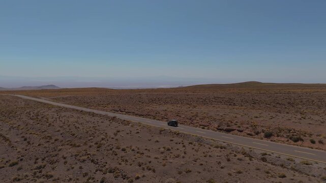 Compact offroad capable suv driving along remote highway across the Atacama Desert landscape, drone panoramic rearview follow