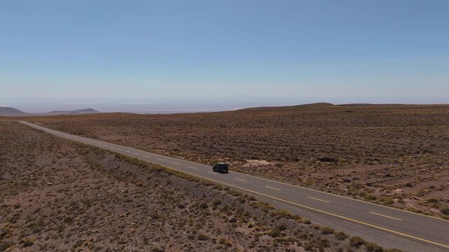 Compact offroad capable suv driving a lonely highway, Atacama Desert region, drone rearview tracking solo traveler