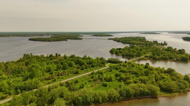Drone side pullback revealing an island along Long Sault Parkway with the scenic roadway crossing the St. Lawrence River and additional islands in the distance.