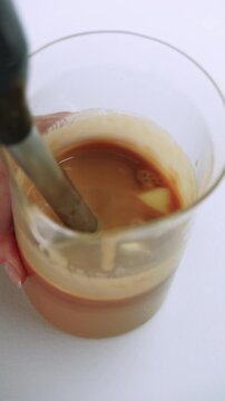 Vertical video. Kitchen appliance. Blending process. Chef hand mixing brown liquid butter in beaker with professional electric device.