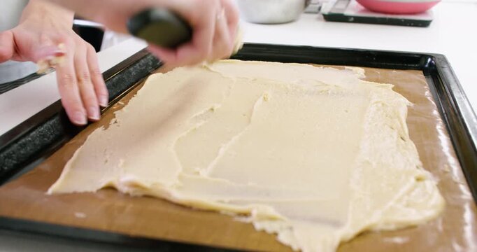 Baking process. Spreading dough. Confectioner woman hand flattening dessert recipe ingredient on silicone mat with metal kitchen tool.
