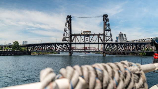 View of the Steel Bridge spanning the Willamette River with industrial structures in the background under a blue sky in Portland, Oregon, United States.