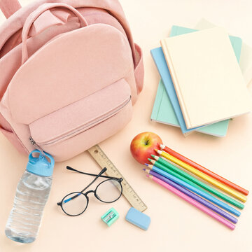 Pink backpack surrounded by notebooks, colored pencils, apple and stationery items on a light background. Arrangement leaves copy space for text and educational layout uses.