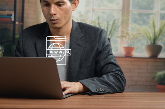 Businessman Working on Laptop at Desk in Office with Green Plants and Brick Wall Background