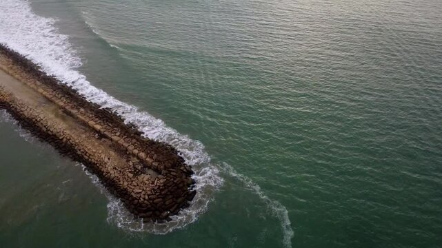 Drone's sensing shot with panoramic development from the pier to San Mateo beach, while the waves crash against the large stones of the pier set upon the emerald green waters of the Pacific Ocean at m