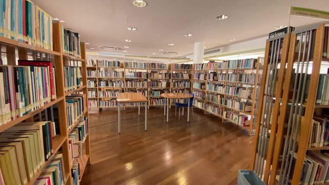 Bright library interior featuring long wooden bookshelves filled with various books, offering a quiet space for learning and research