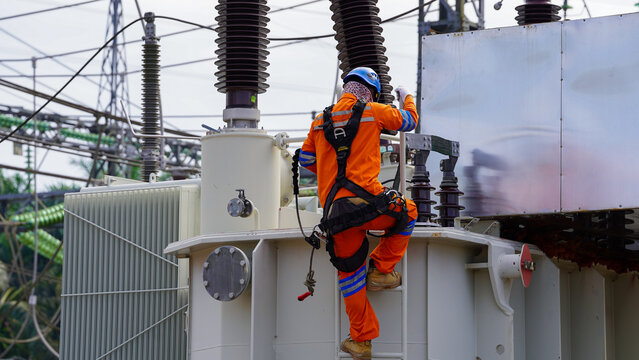 Electrical technician climbing transformer during maintenance work