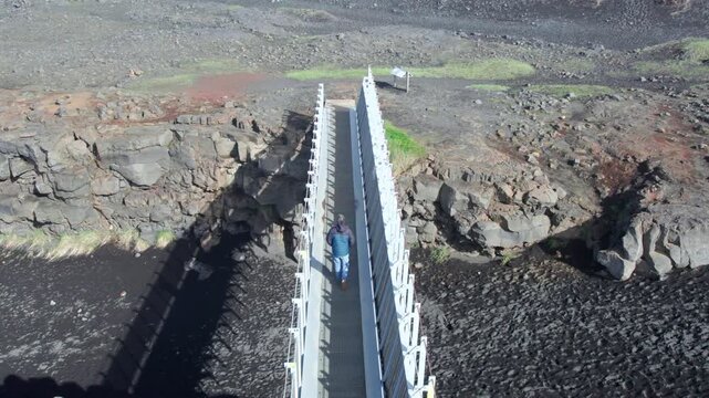 Visitor strolling along the Mid Atlantic Ridge footbridge that links the Eurasian and North American tectonic plates in the Reykjanes Peninsula, Iceland.