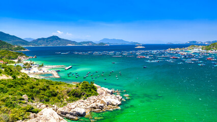 Naklejka premium Aerial view of Cam Ranh Bay, Vietnam, featuring crystal-clear turquoise waters, fishing farms, sandy beaches, and surrounding mountains. 