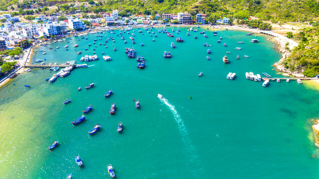 Breathtaking aerial view of Vinh Hy Bay, Vietnam, featuring emerald waters, colorful fishing boats, coastal villages, and rugged mountains. 