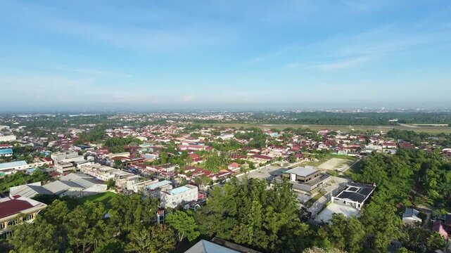 Cinematic aerial view of a small town in Indonesia, featuring residential neighborhoods, local roads, tropical greenery, and a peaceful community atmosphere.