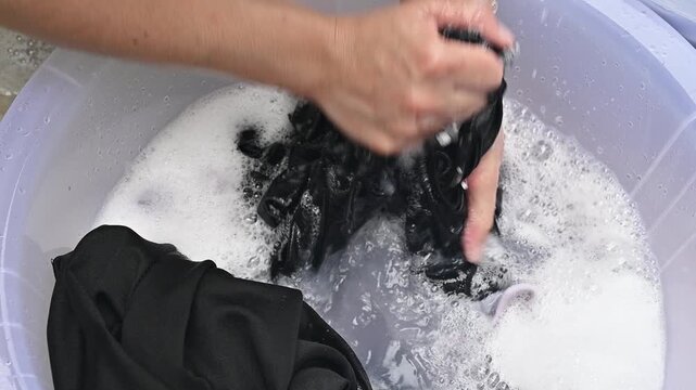 Cropped shot view of woman washing black clothes by hands. Washing by hand is therefore a great way to keep them looking new and fresh for longer.