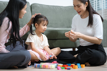 Fototapeta premium Happy Asian mother and curious young girl enjoy creative learning activities at home. Family bonding, child development, education, playtime, and weekend lifestyle.