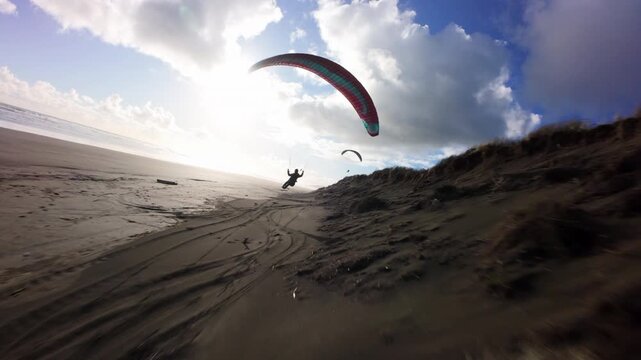 Paraglider flying above coastal sand dunes in New Zealand