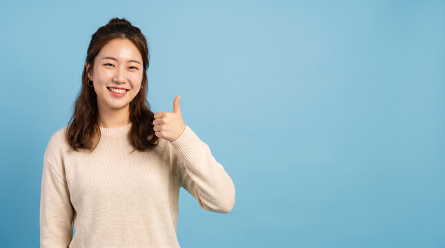 Smiling young woman showing thumbs up on blue background