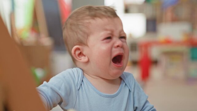 Toddler boy crying with open mouth, tears and outstretched arm reaching for a toy handle in a building play area; distress need.