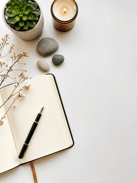 Mindfulness flat-lay with open journal, pen, succulent, river stones, candle and dried flowers on white background, copy space. 
