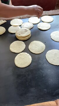 Guatemalan woman preparing handmade corn tortillas from fresh masa dough and placing them on hot griddle. Traditional cooking process showcasing local cuisine, culture and authentic food preparation.