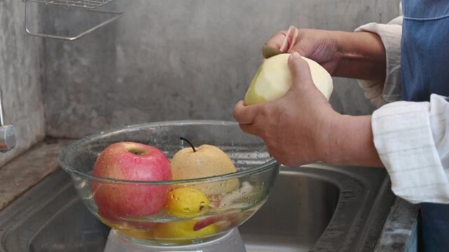Peeled apple pear fruit peeled apple fruit bowl apple pear pear fruit kitchen sink peeling hands female hands knife stainless steel glass bowl water fresh fruit preparation countertop home kitchen