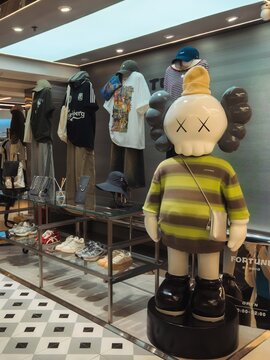 GUANGZHOU, CHINA - JUNE 18, 2026: A modern streetwear clothing store display window featuring a large designer KAWS companion style vinyl figure on a checkerboard floor in a shopping mall.