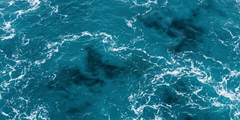 An aerial view captures the dynamic motion of deep blue ocean water, with frothy white waves creating intricate patterns on the surface, hinting at the depths below. © Artova LaLa