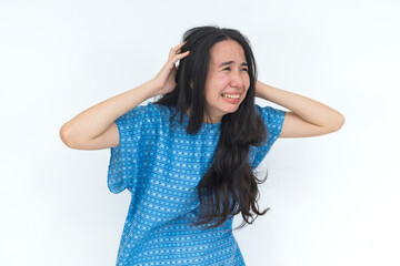 Fototapeta premium A young Filipino female patient in a hospital gown holds her head in distress, expressing anxiety, emotional overwhelm, stress, and mental health challenges.
