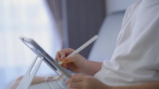 Close-up of a person using a digital tablet with a stylus in an indoor setting, emphasizing technology, digital communication, and modern work environment