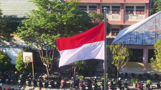 The Indonesian red and white flag flutters elegantly in a school yard with motorcycles parked in the background.