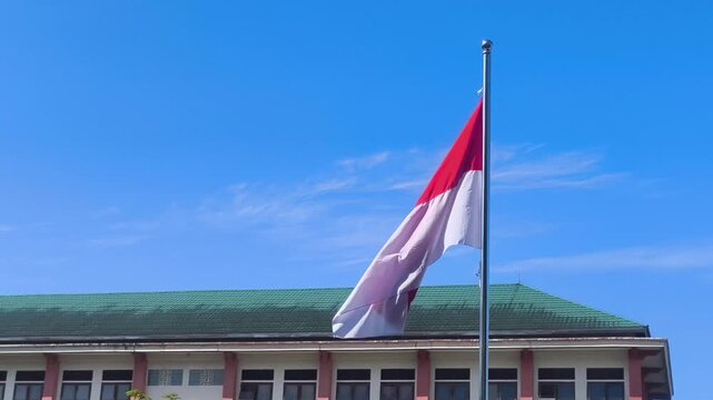 The red and white flag of Indonesia blows in the wind on a bright, sunny day.