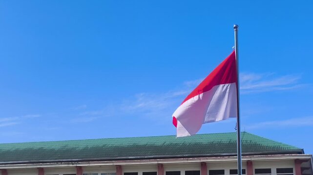 A beautiful view of the Indonesian national flag waving gently in front of a green-roofed building.