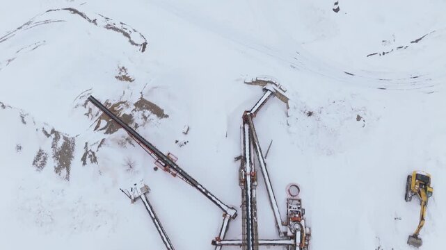 Industrial conveyor systems span a snow covered gravel pit with loader and worker visible.