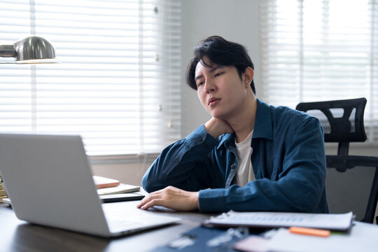 Young Asian man feeling tired and stressed while working from home office with laptop at desk