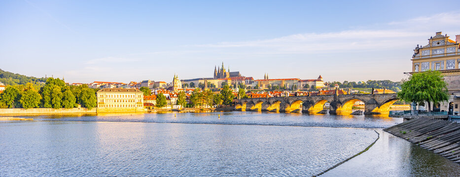 Early morning light casts a warm glow over Prague Castle and Charles Bridge. The Vltava River reflects the cityscape while the historic architecture stands majestically in the background.