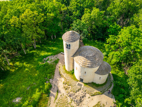 Visitors explore the ancient Rotunda of Saint George on Mount Rip, surrounded by green trees. The structure features two distinct towers and is a historical site attracting tourists.