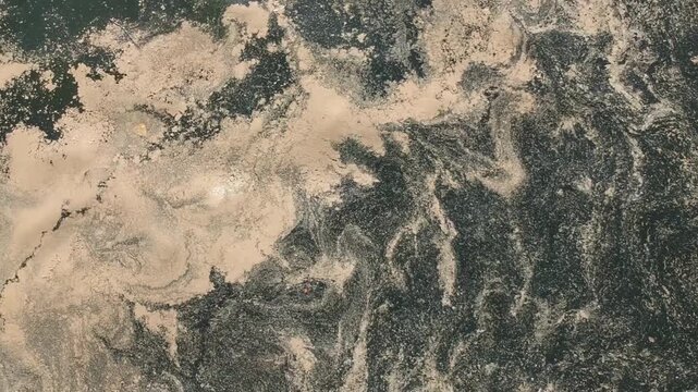 Polluted water surface with swirling patterns of dark sludge and light brown sediment or algae