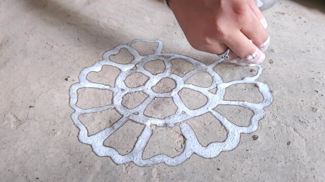 Woman drawing a traditional Rangoli pattern on the floor using rice and water mixed white paint. This beautiful handmade floral design is commonly created during Hindu festivals, religious ceremonies