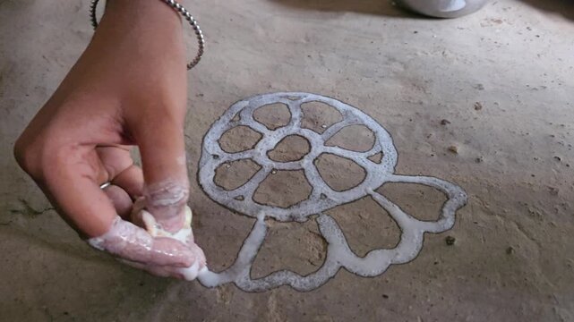 Woman drawing a traditional Rangoli pattern on the floor using rice and water mixed white paint. This beautiful handmade floral design is commonly created during Hindu festivals, religious ceremonies